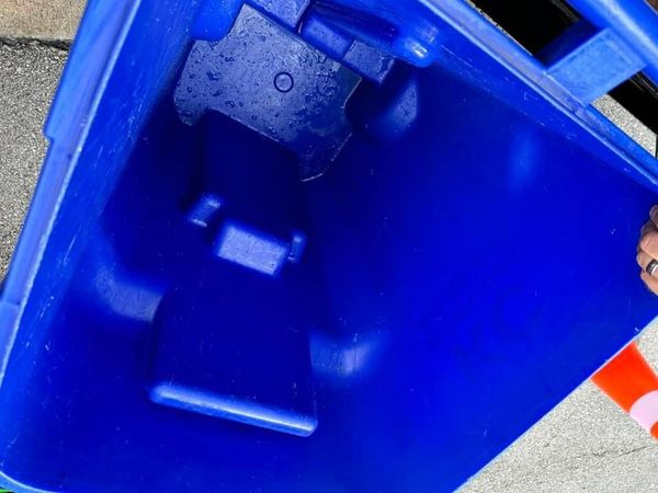 A person is holding a blue trash can on the sidewalk.