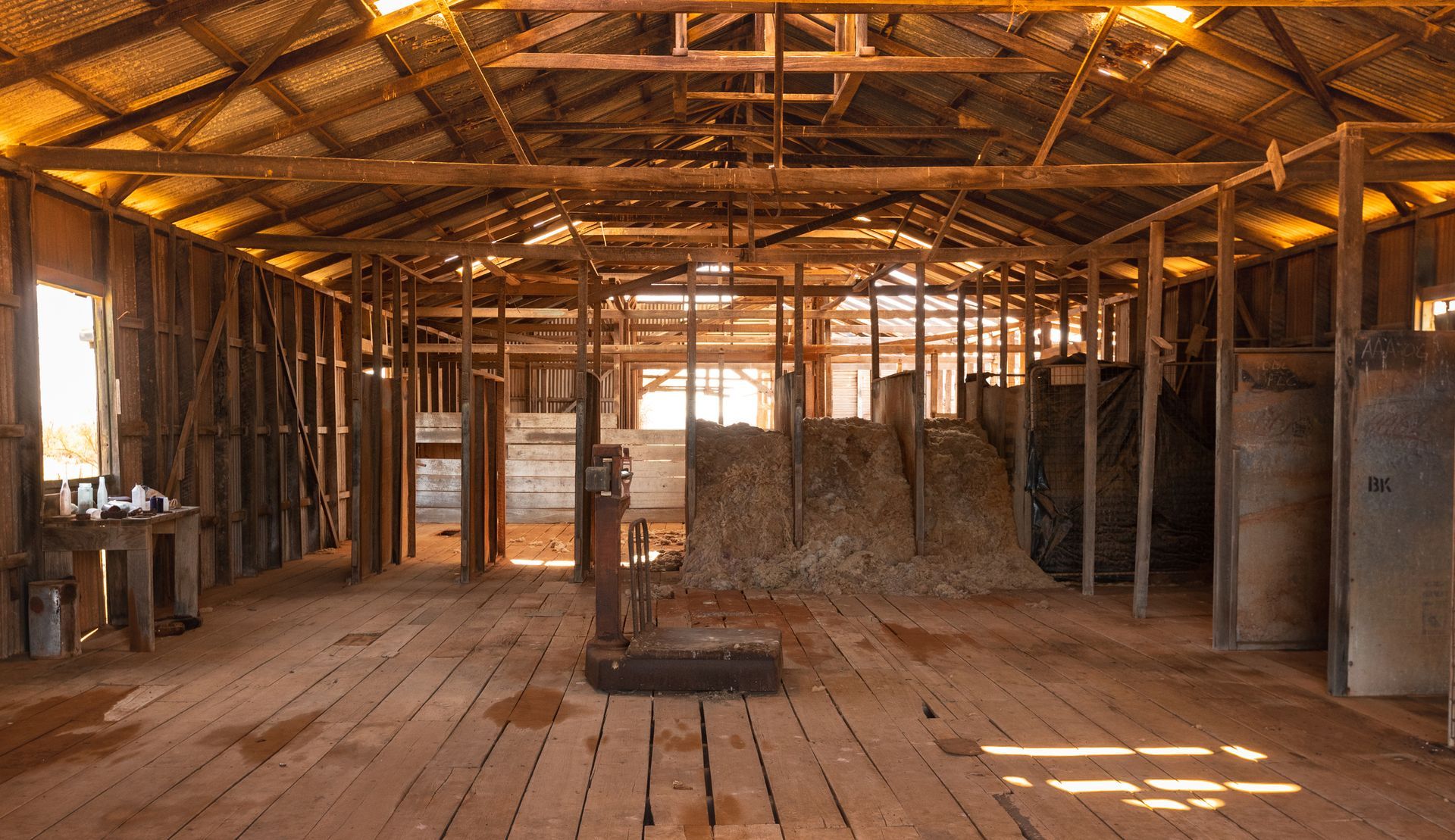 Interior view of an old, wooden barn with hay bales, weathered walls, and bright sunlight.