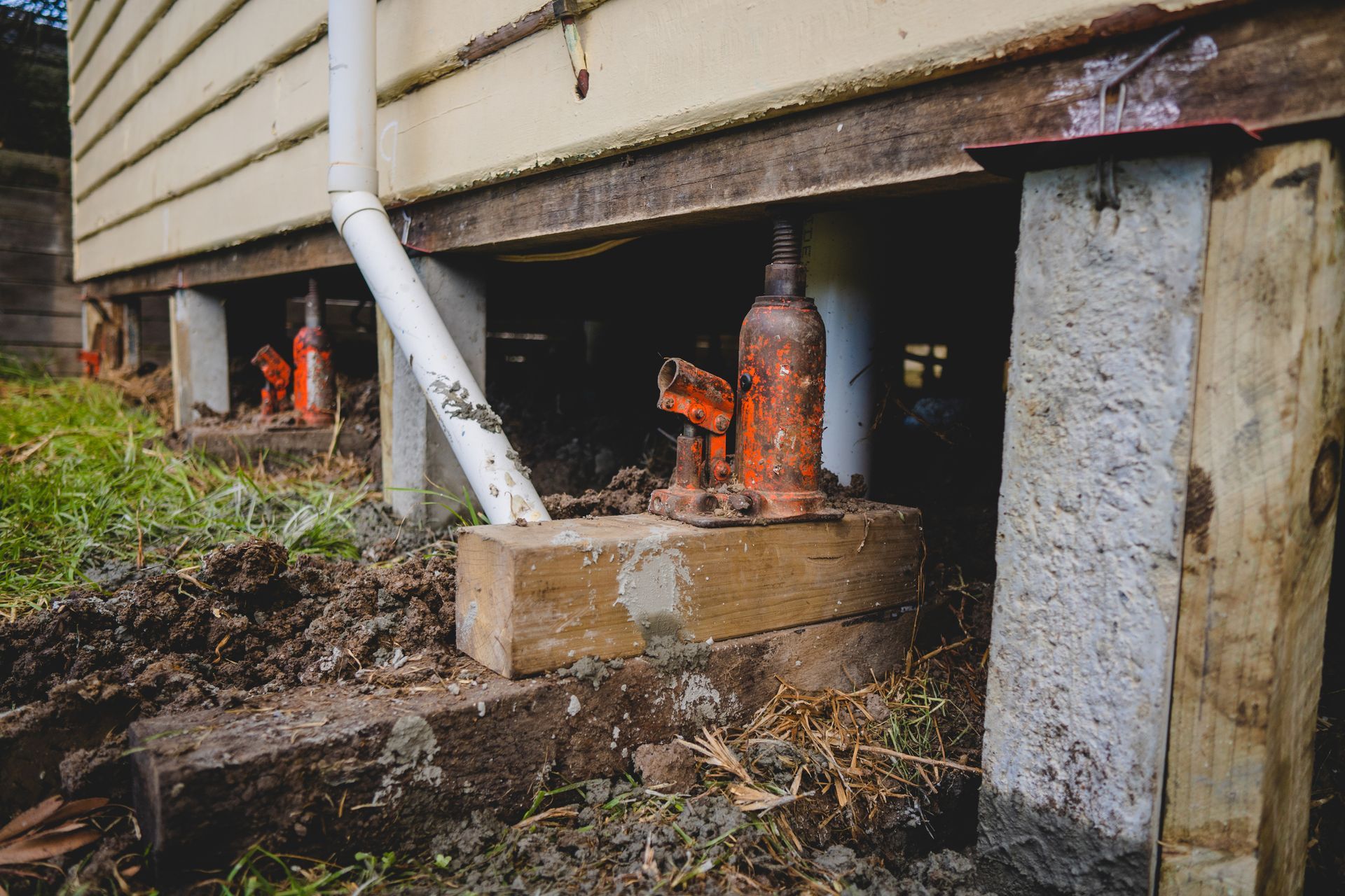 A series of jacks under a clapboard house during the re-stumping process.