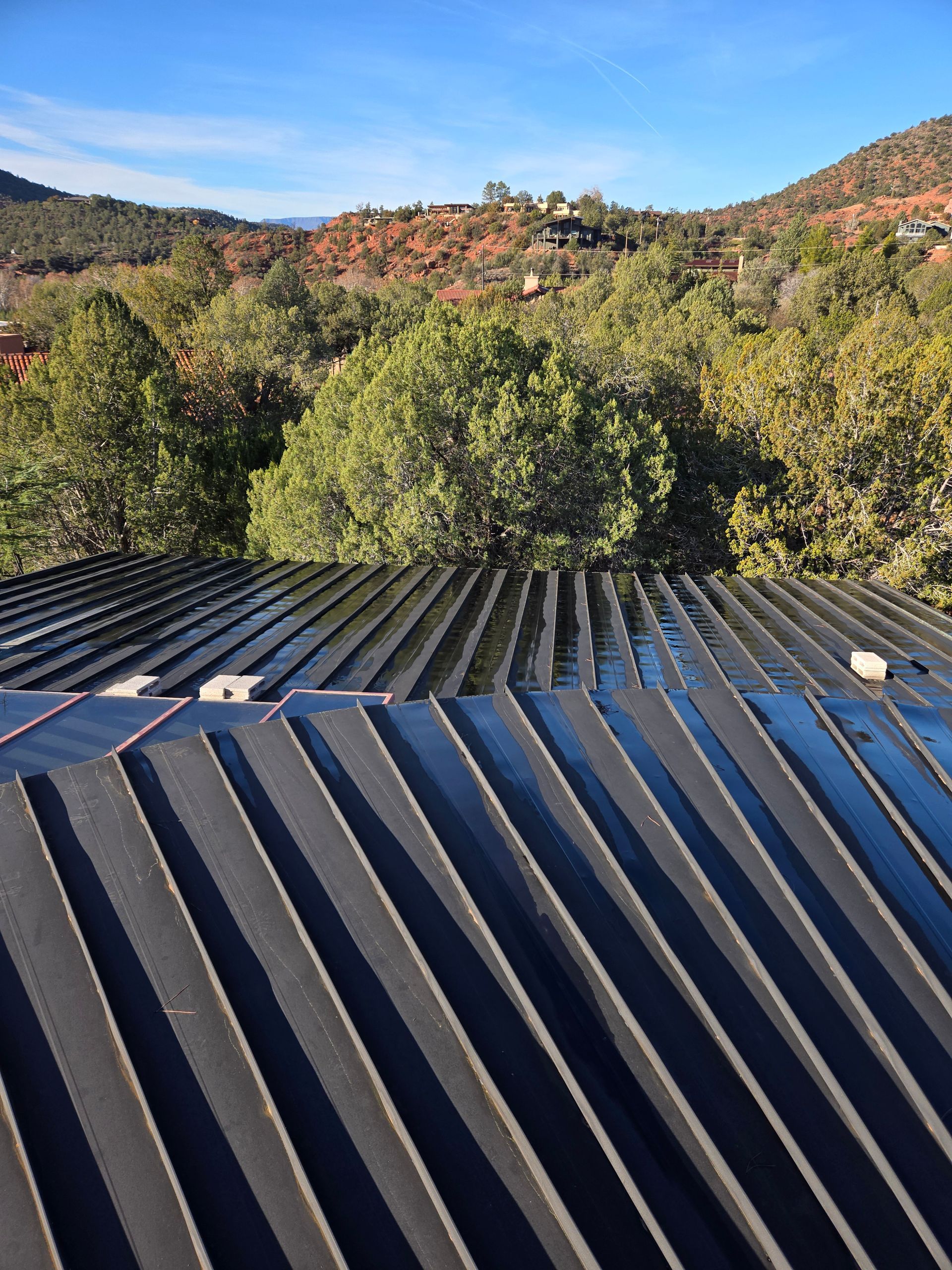 Black corrugated metal roof with a mountain vista in the background. Blue sky, green trees, and red rocks.