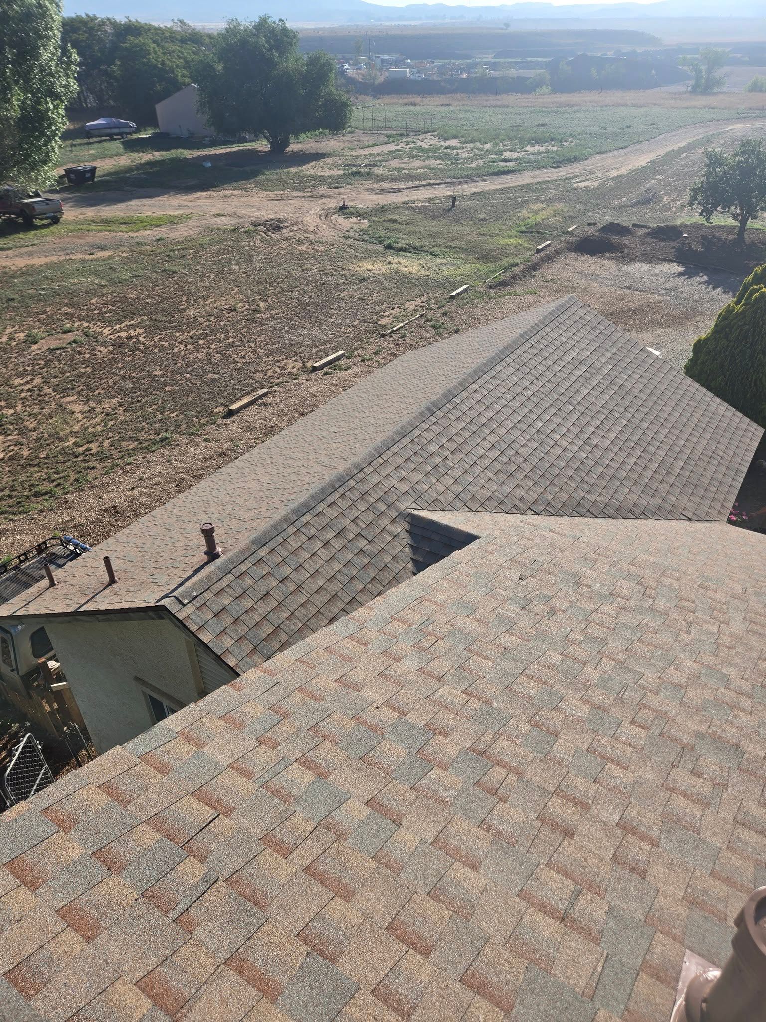 Overhead view of several roofs with brown shingles. Dry, brown landscape in background with trees.