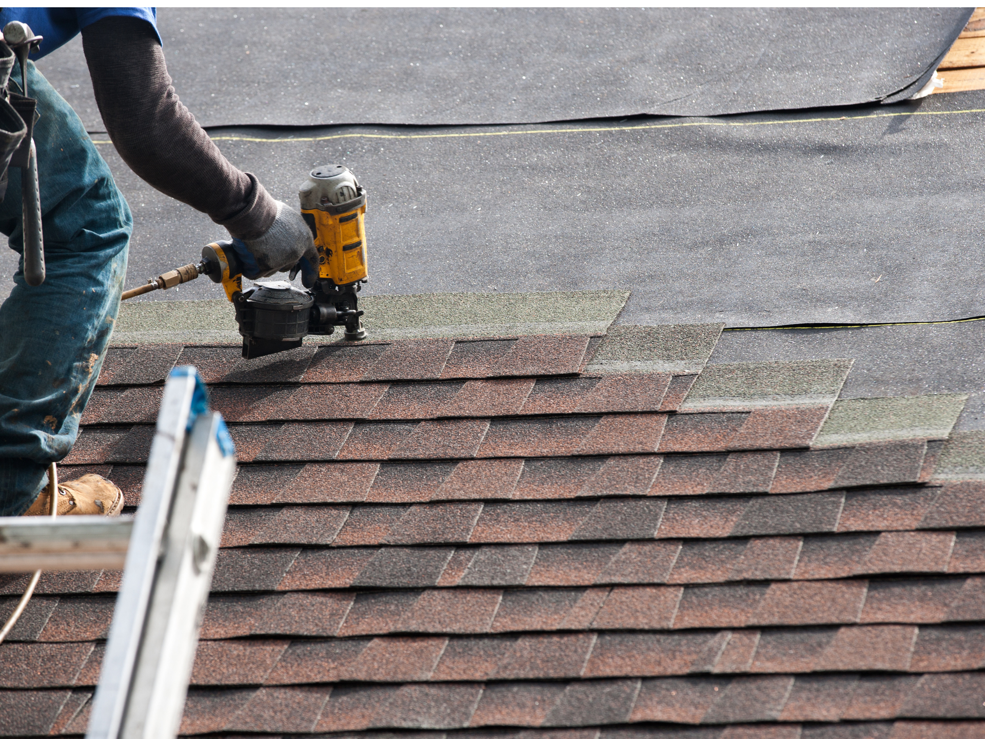 Roofer using a nail gun to install asphalt shingles on a roof.