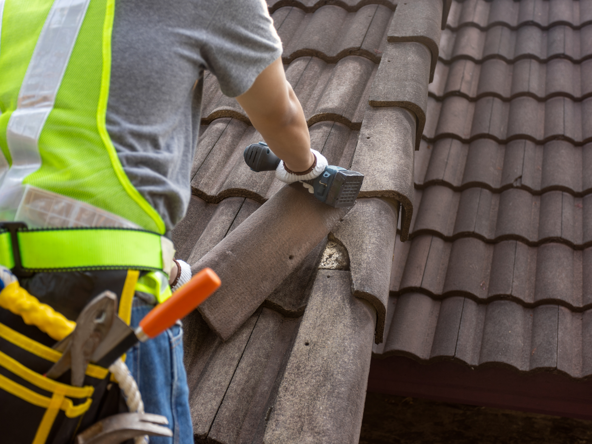 Roofer in safety vest removes tile from a clay tile roof.