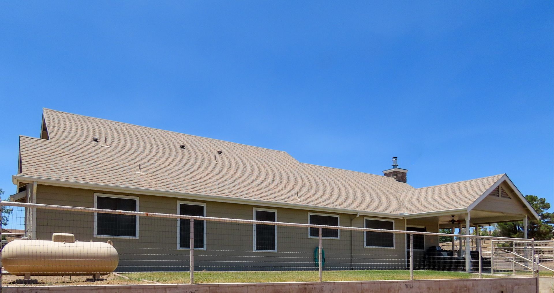 Single-story tan building with a wavy roof and blue sky overhead, seen behind a fence.