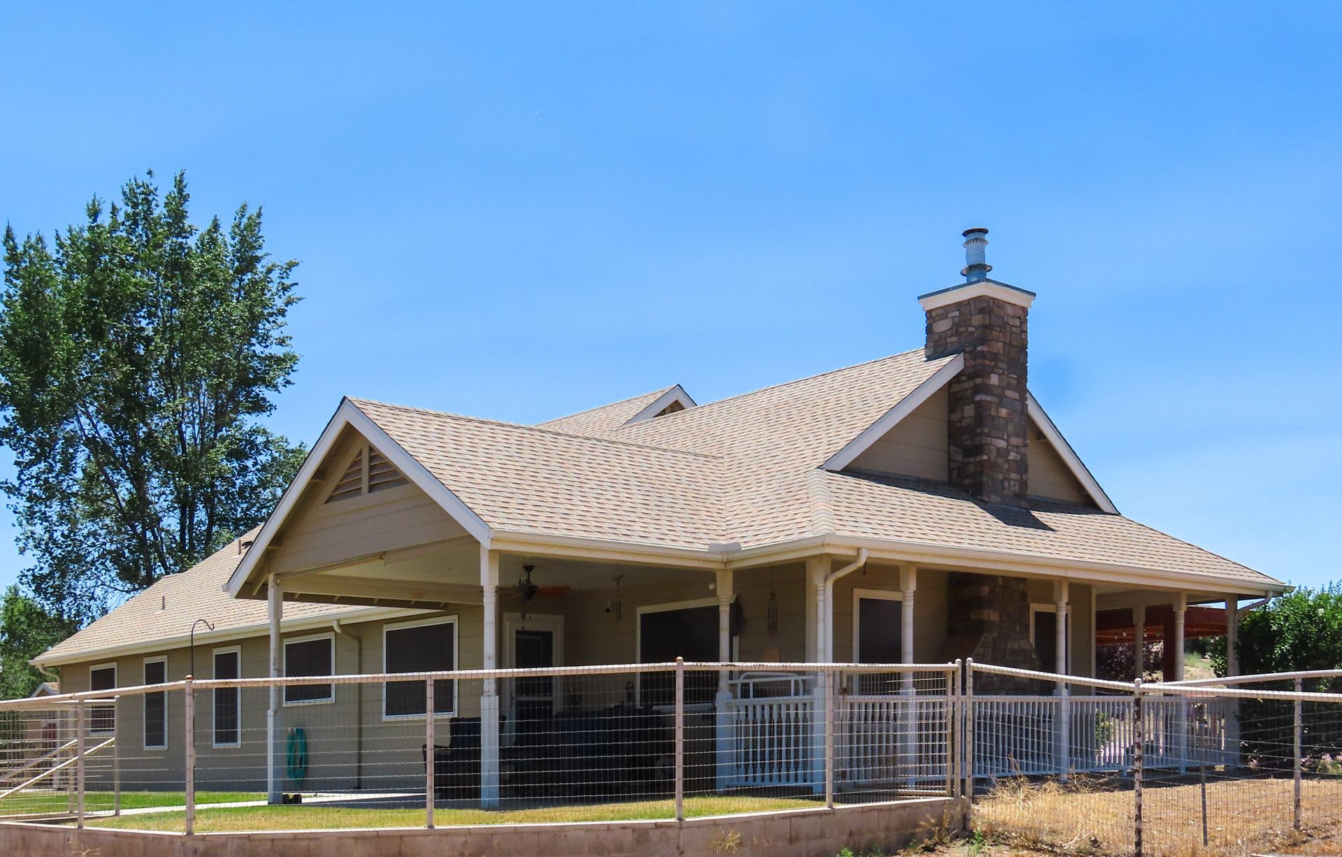 Single-story house with a beige roof, brick chimney, and white porch railing under a clear blue sky