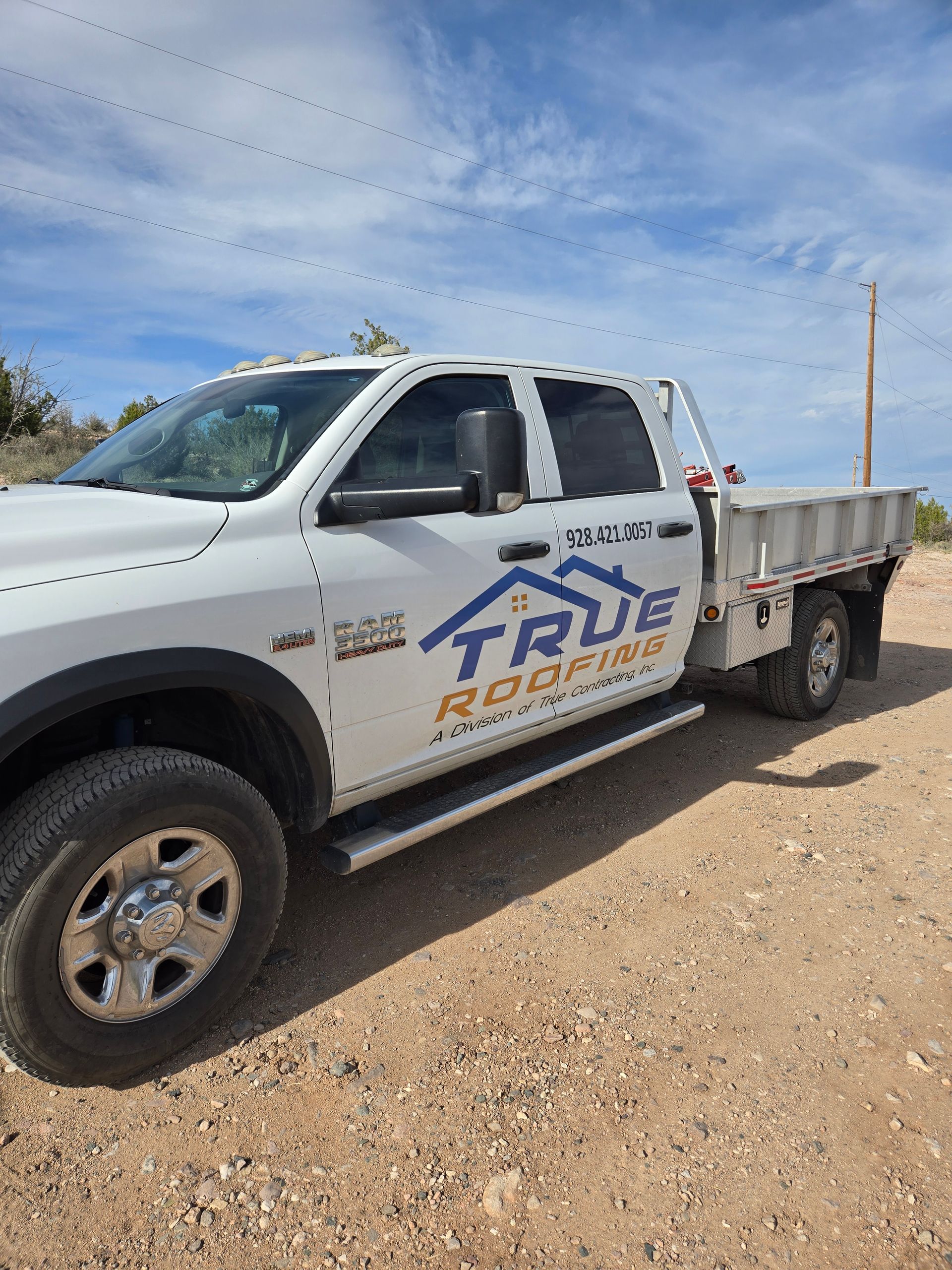 White True Roofing truck parked on a dirt road under a cloudy sky.