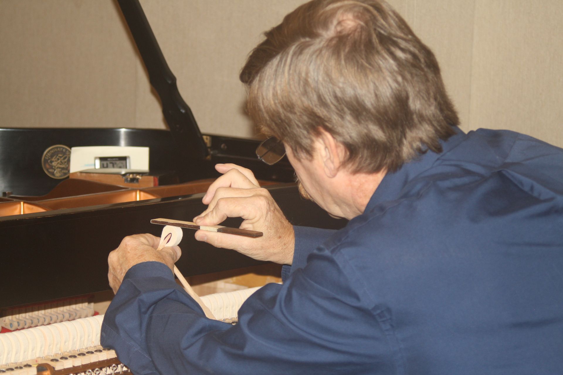 A man in a blue shirt is working on a piano