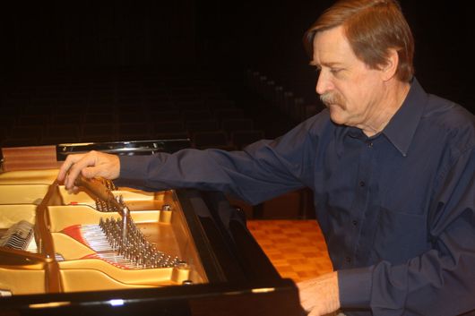 A man in a blue shirt is working on a piano