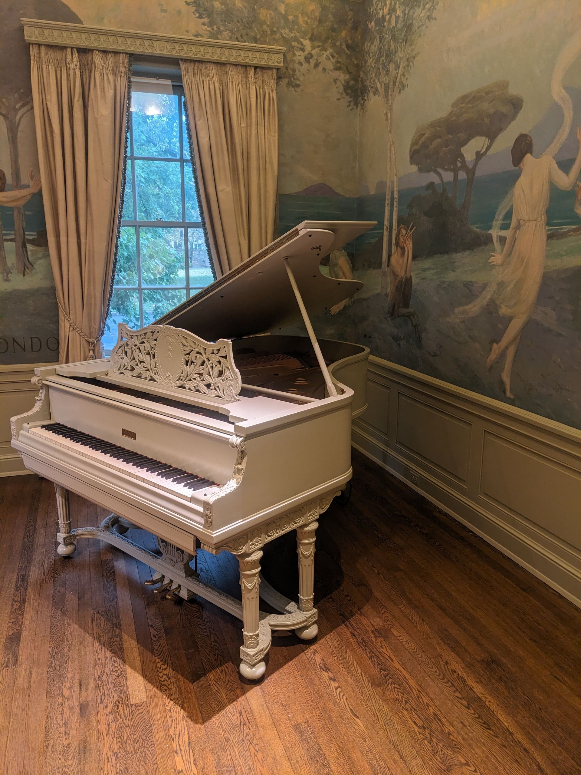 A white grand piano is sitting in a room with a painting on the wall.