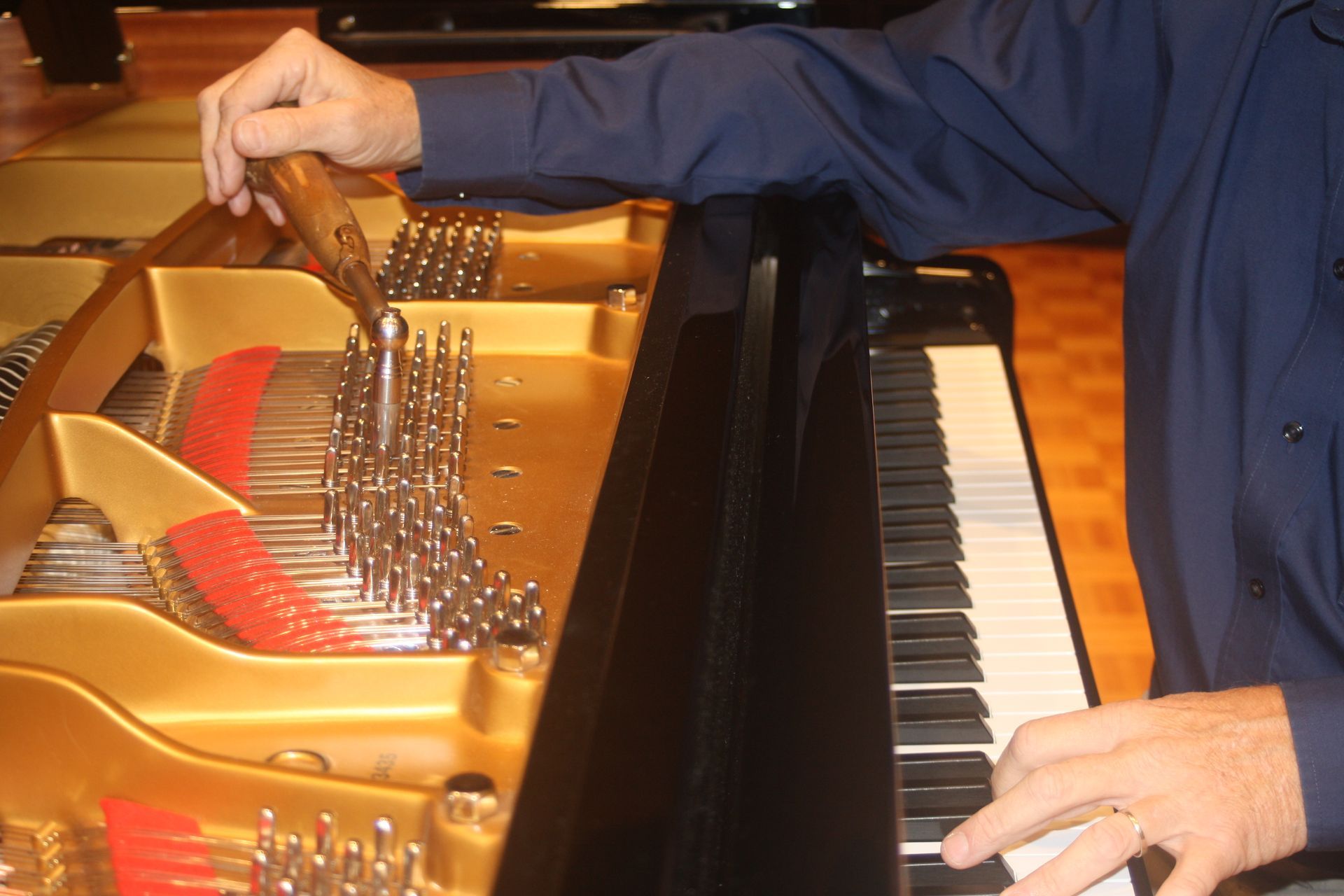 A man in a blue shirt is working on a piano