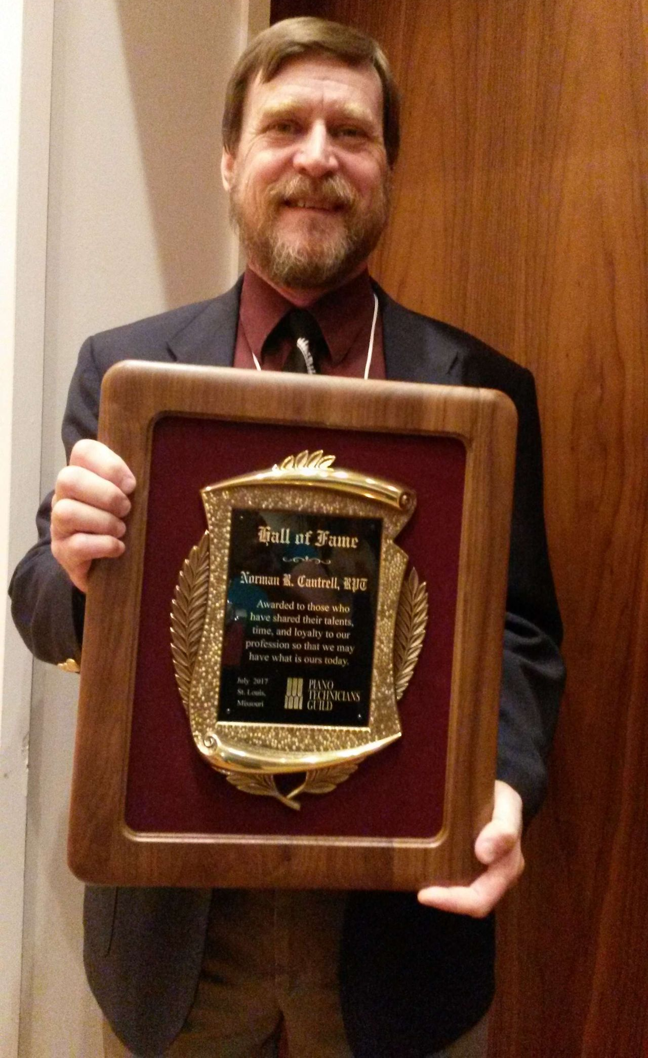 A man in a suit and tie is holding a framed plaque