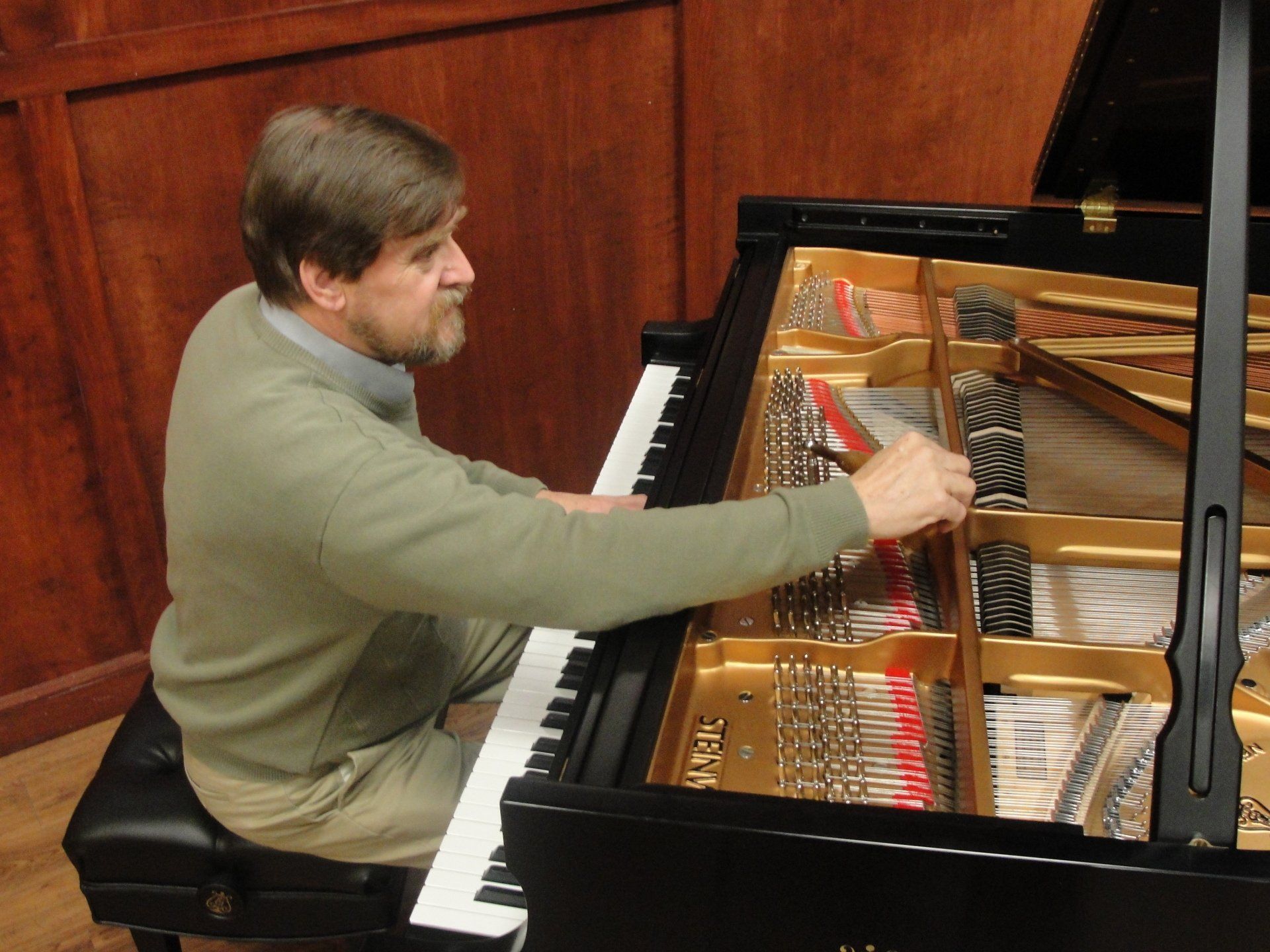 A man in a green sweater is playing a piano