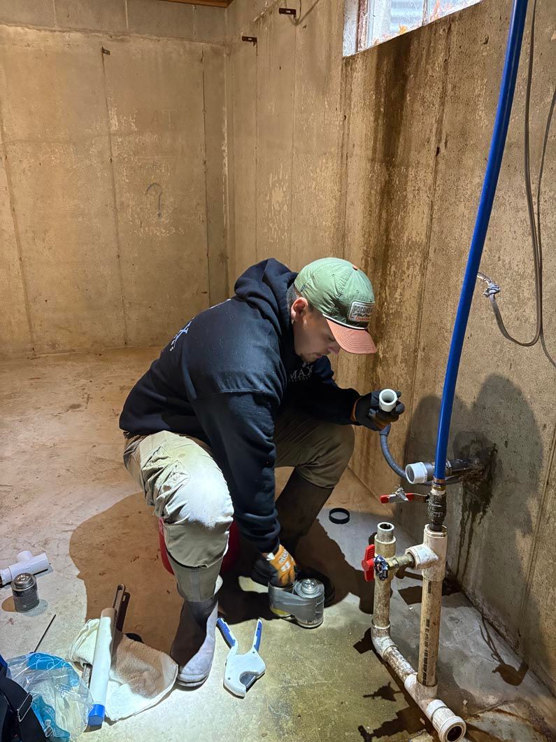 A man is kneeling down in a room working on a pipe.