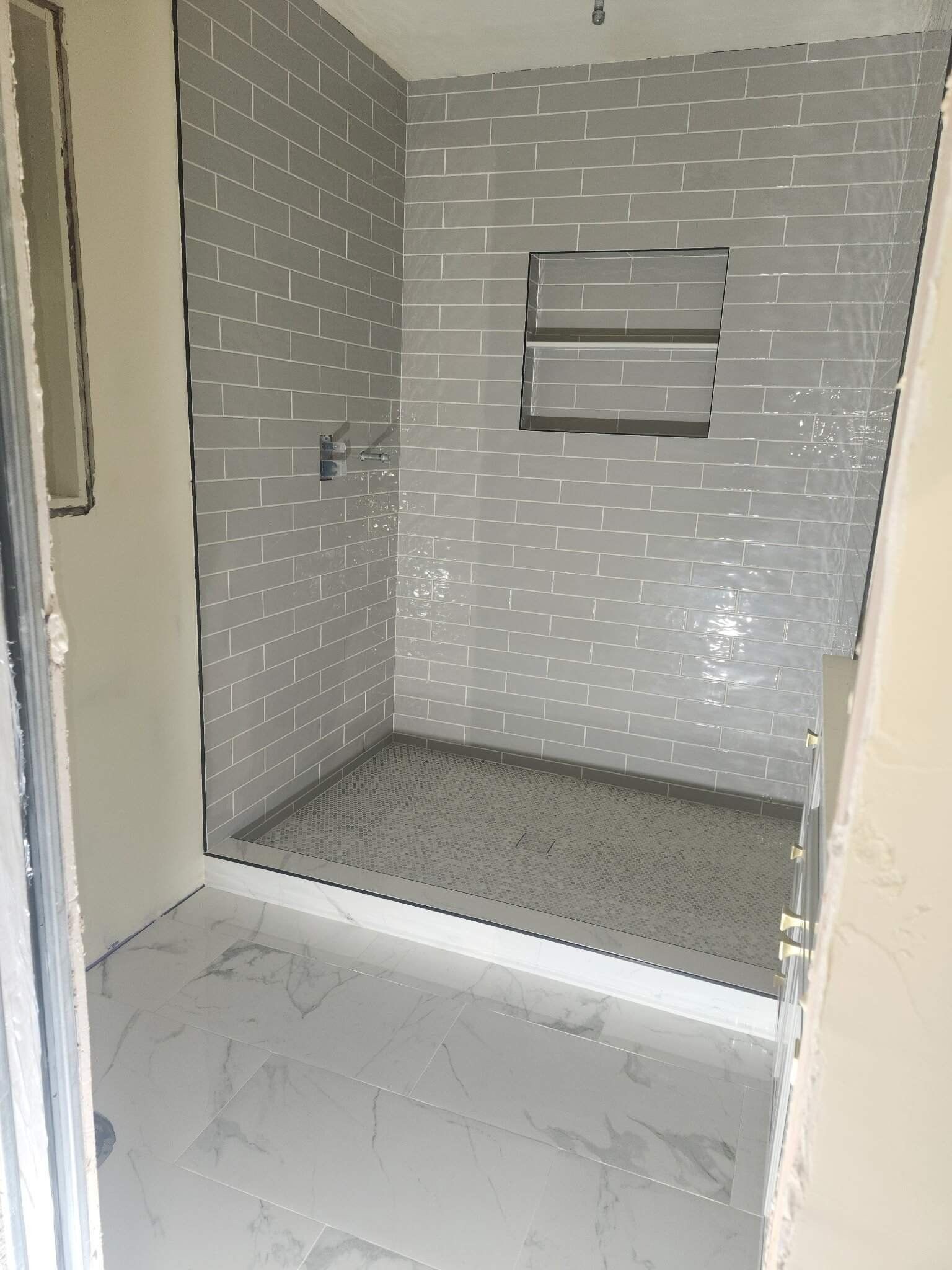 Empty gray-tiled shower stall with built-in shelf and white floor tiles