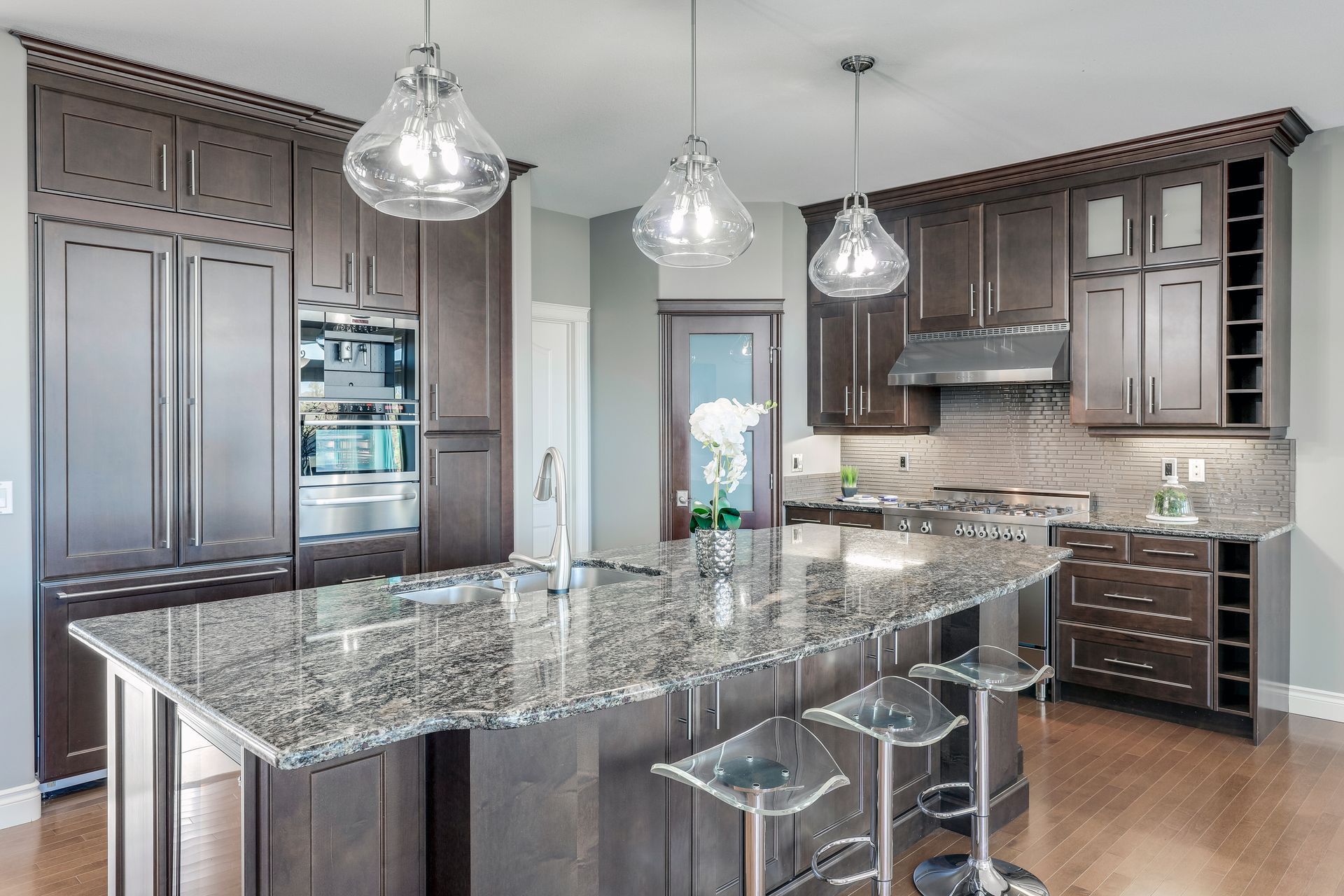 Modern kitchen with dark wood cabinets, granite island, pendant lights, and stainless steel appliances