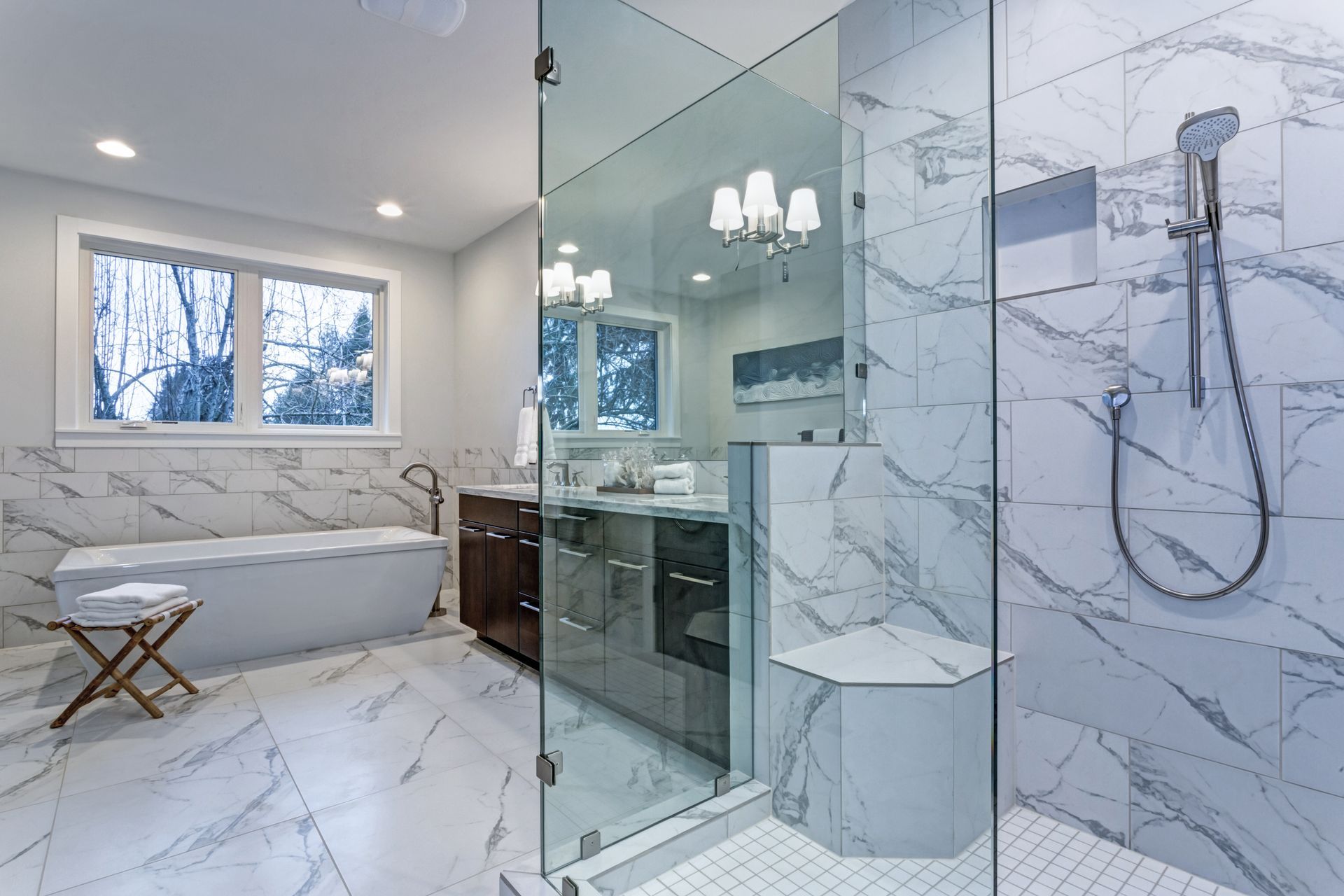 Bright modern bathroom with marble tile, glass shower, freestanding tub, and large window