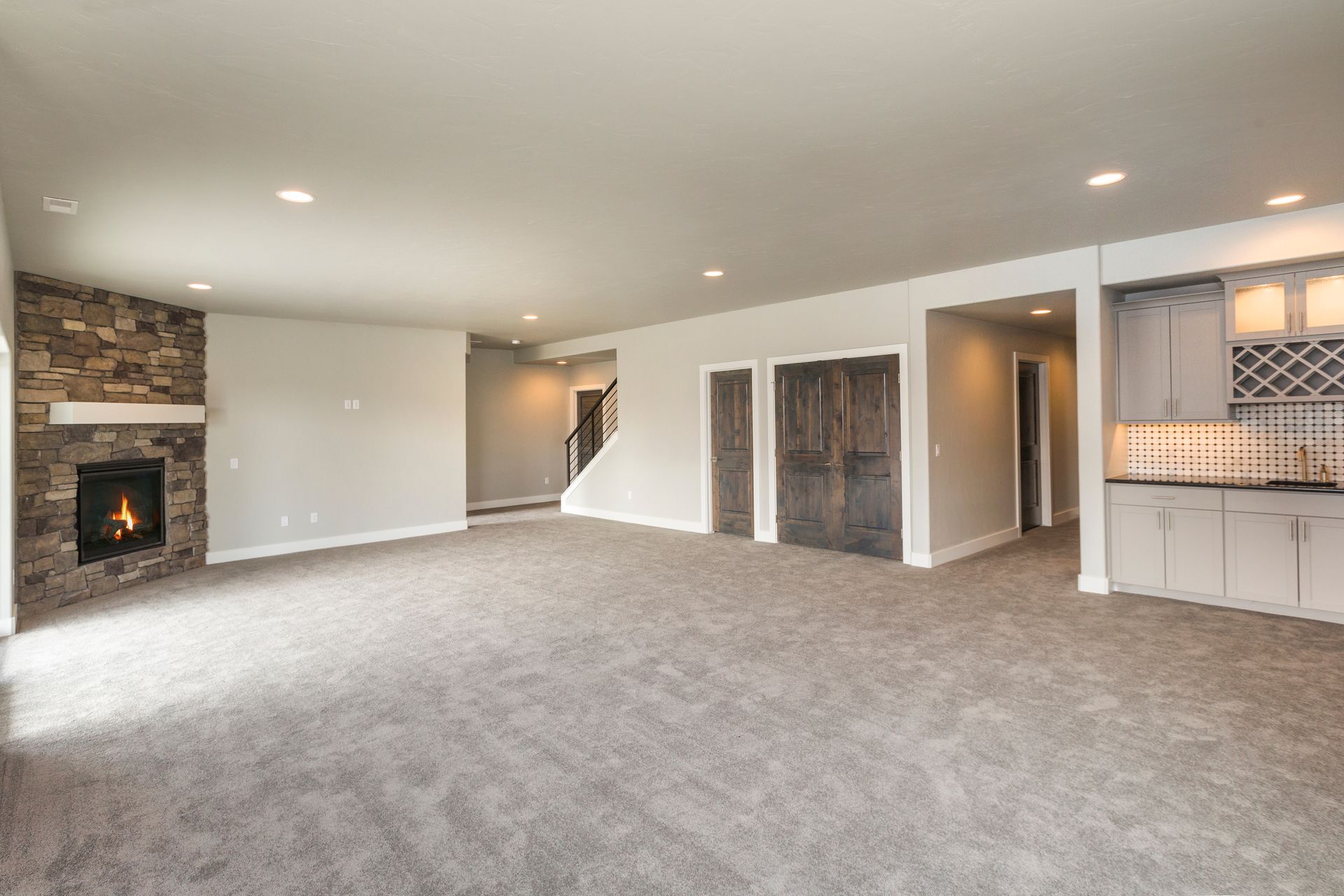 Spacious empty living room with carpet, stone fireplace, recessed lights, and built-in bar area
