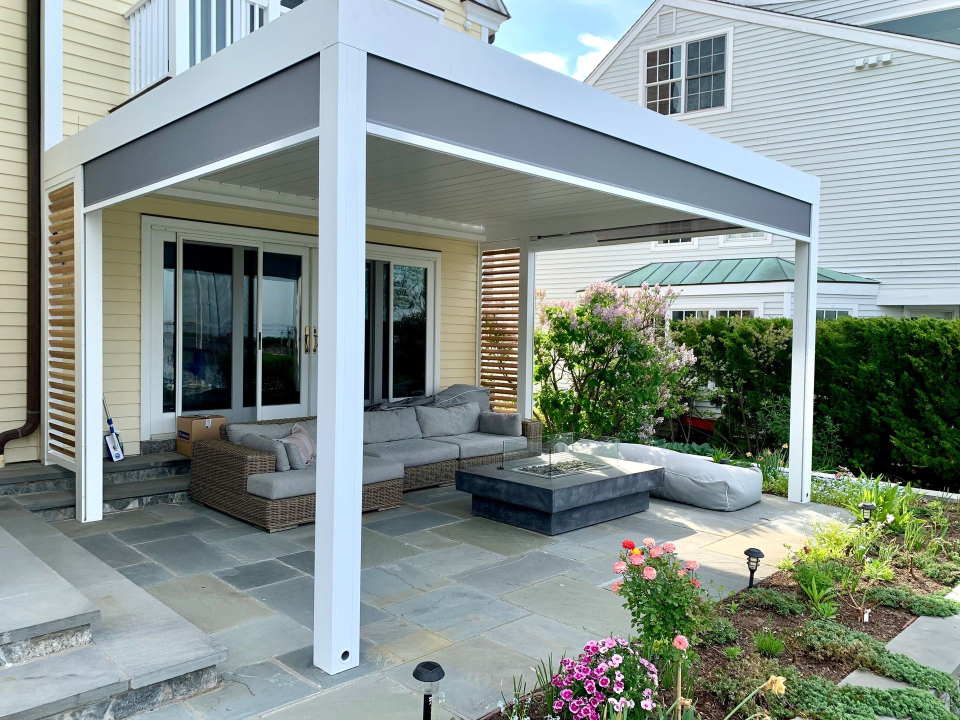 Backyard patio with a white pergola, outdoor seating, and garden flowers beside a house