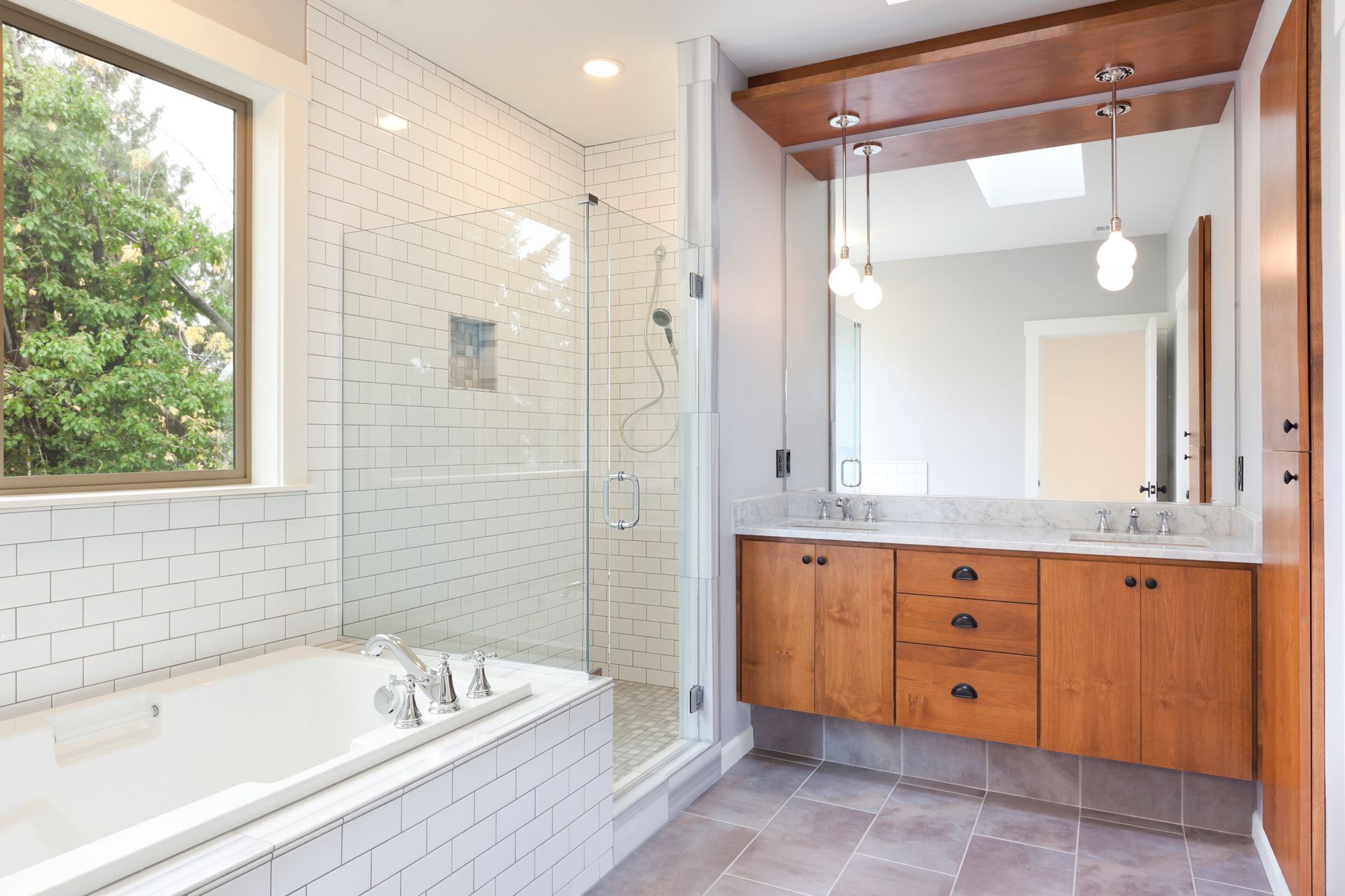 Bright bathroom with white tiled shower, tub, and wooden vanity with large mirror.