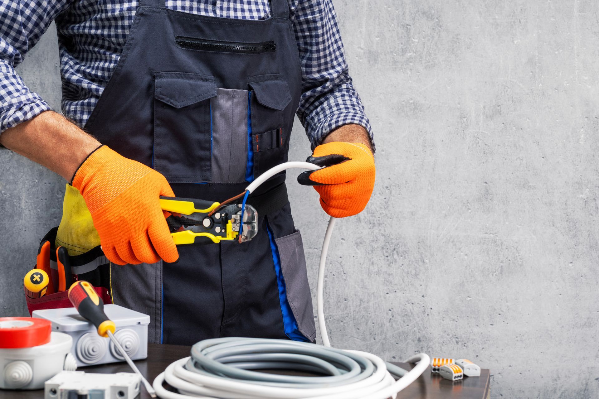 Gloved worker crimping a cable in a workshop, with tools and coiled wire on the table