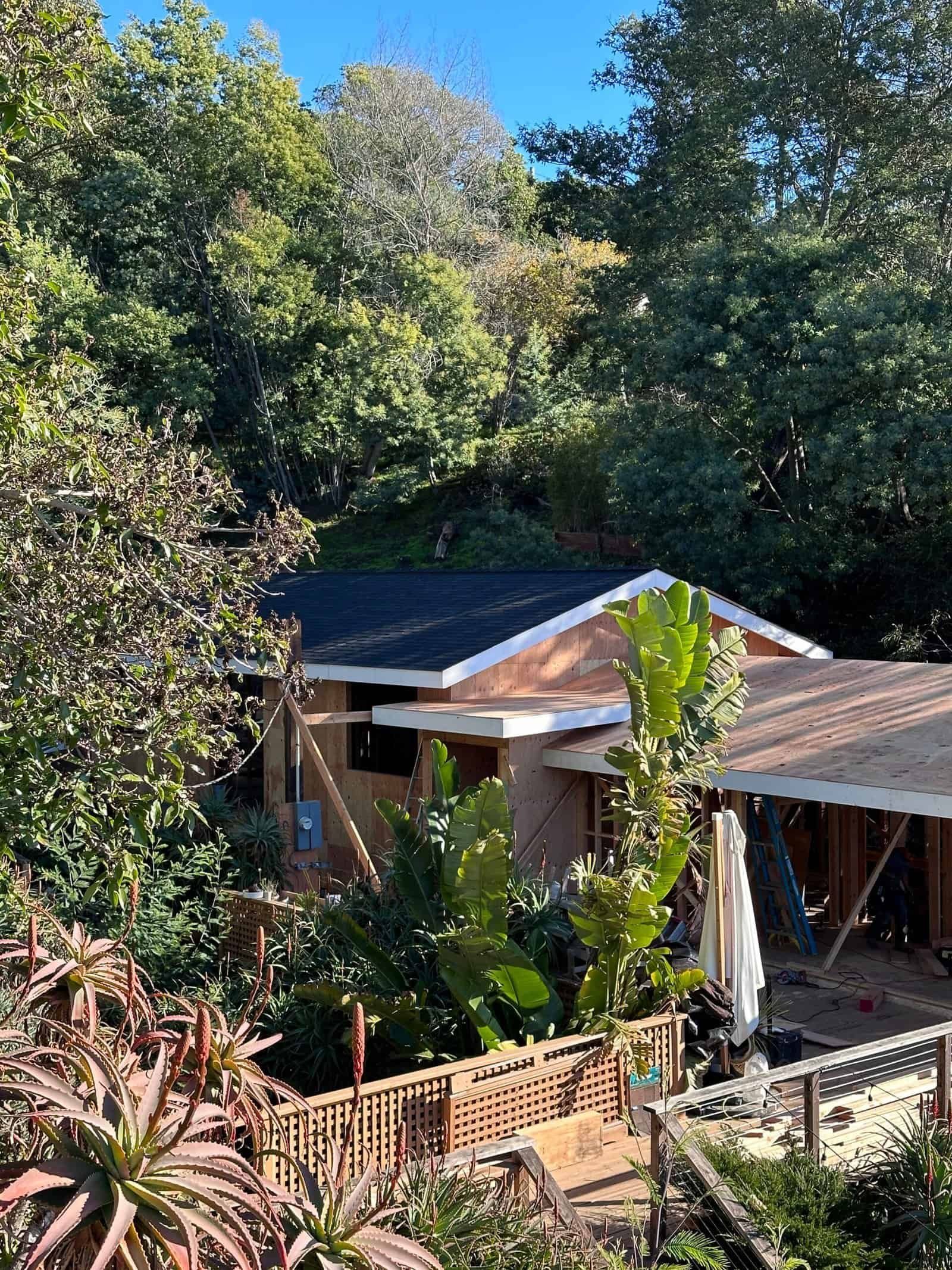 Small house with a dark roof and wooden porch nestled among dense green trees.