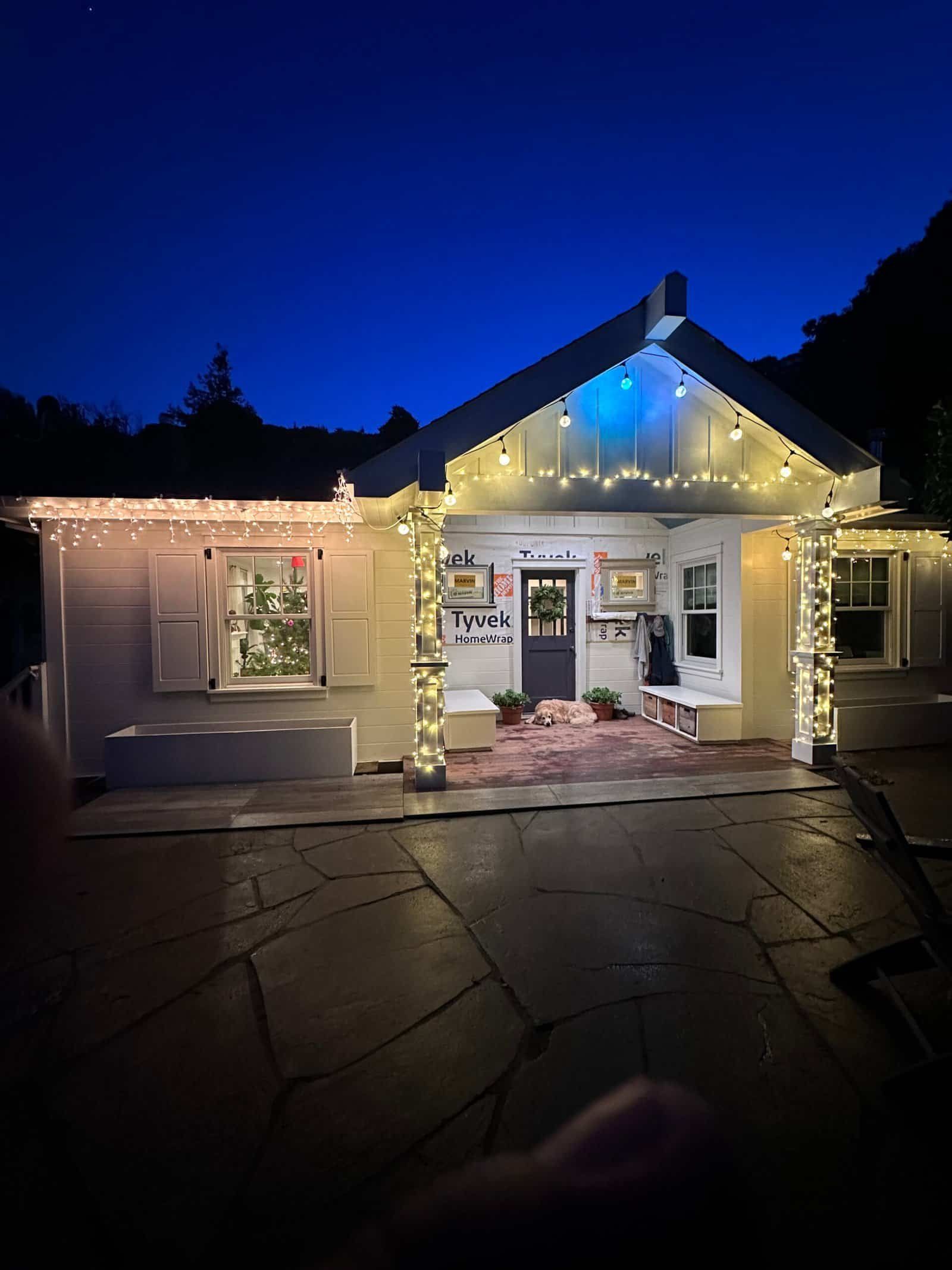 Small house at night decorated with warm white string lights under a deep blue sky