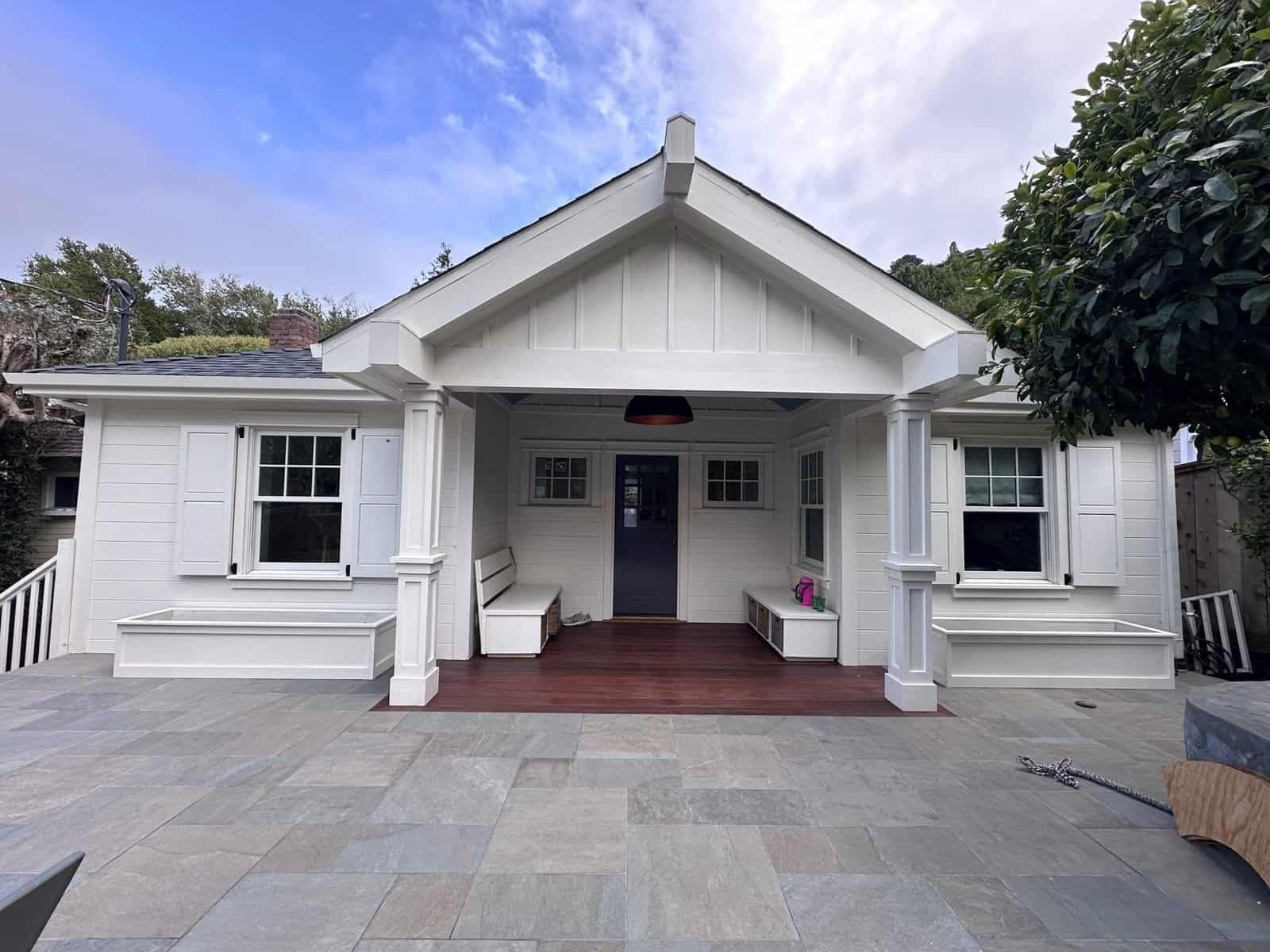 White house with a covered porch, steps, and a paved front courtyard under a cloudy sky