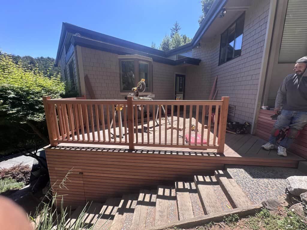 Wooden deck with railing outside a house, with a person standing at the right edge.