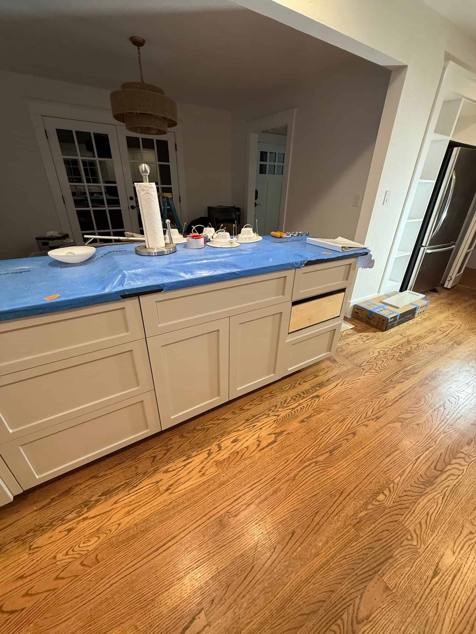 Kitchen island covered with blue tarp and cleaning supplies in a bright home interior