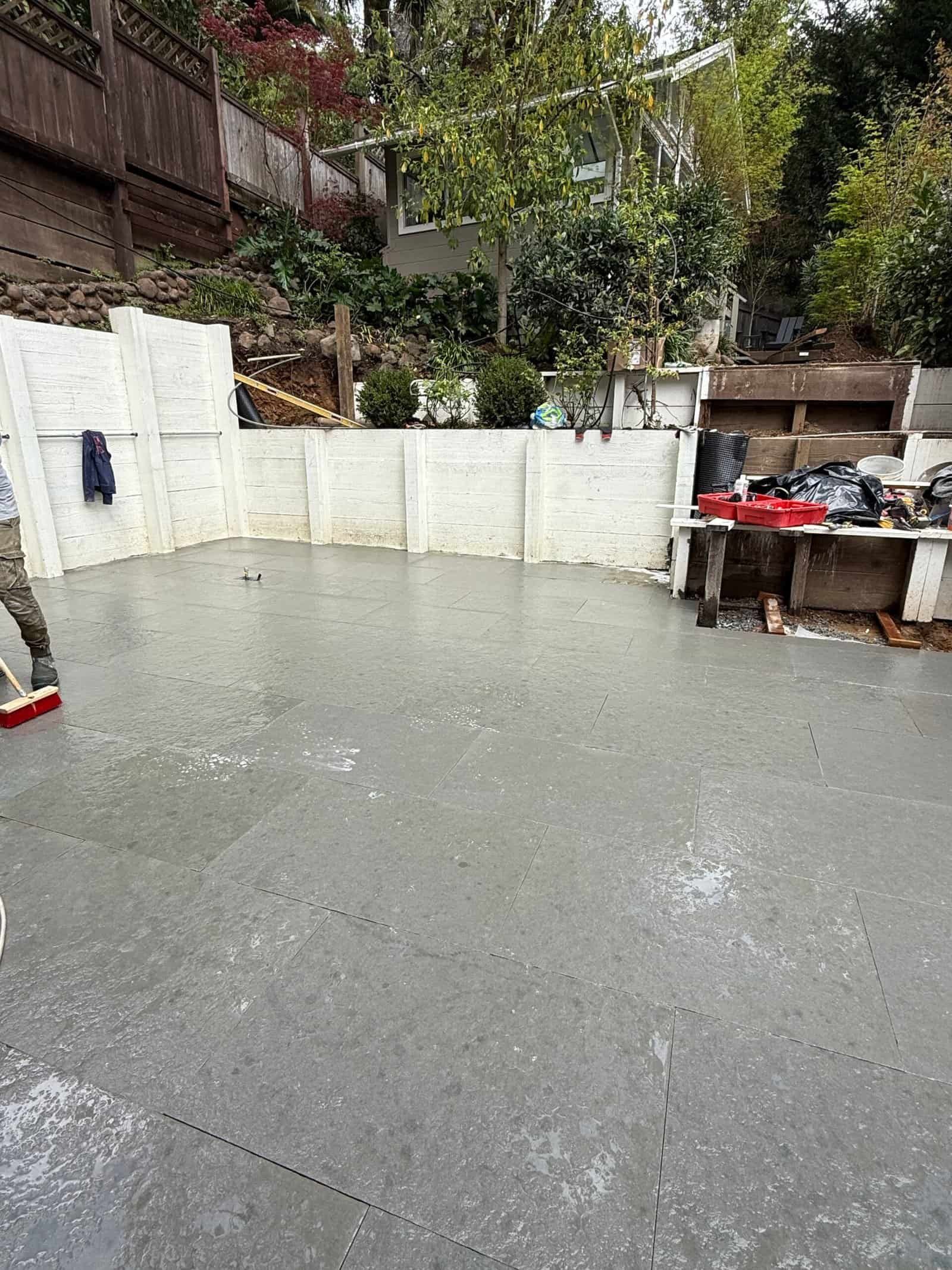 Rain-soaked concrete courtyard with white walls, trees, and a small outdoor table on the right