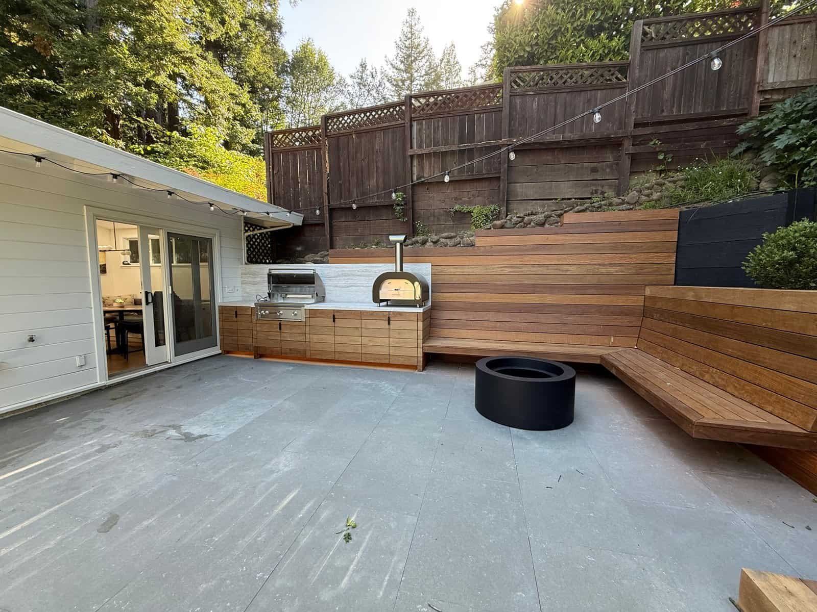 Backyard concrete patio with wood deck seating area and fire pit beside a house
