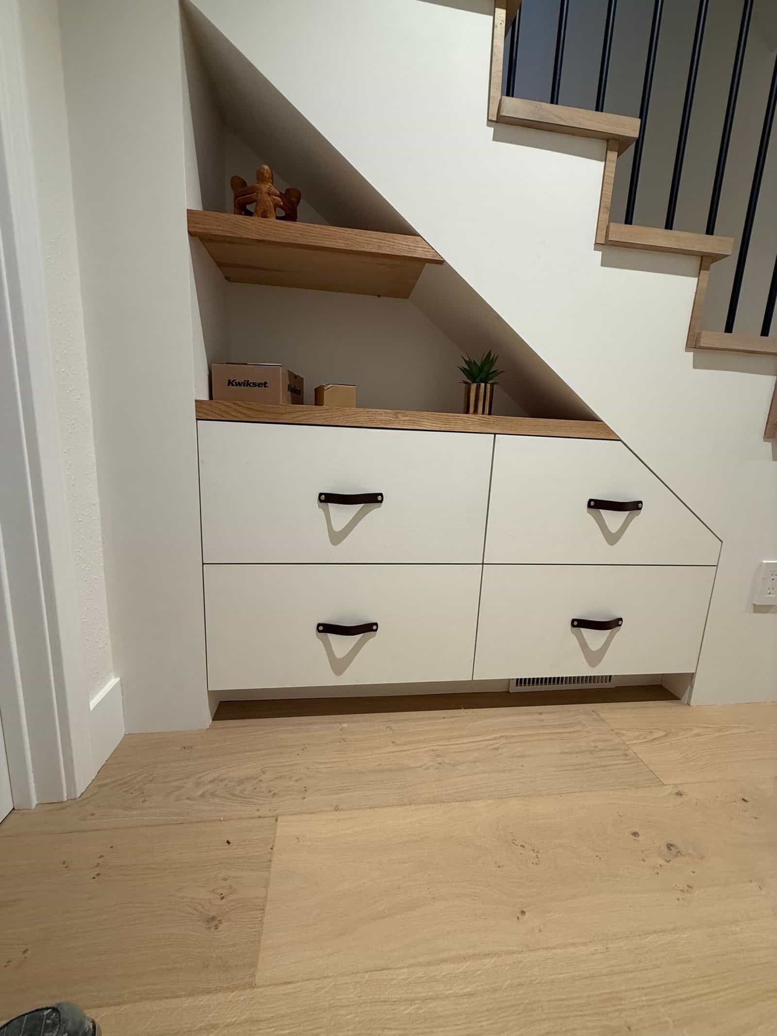 Under-stair storage cabinet with drawers, shelves, and small decor in a hallway