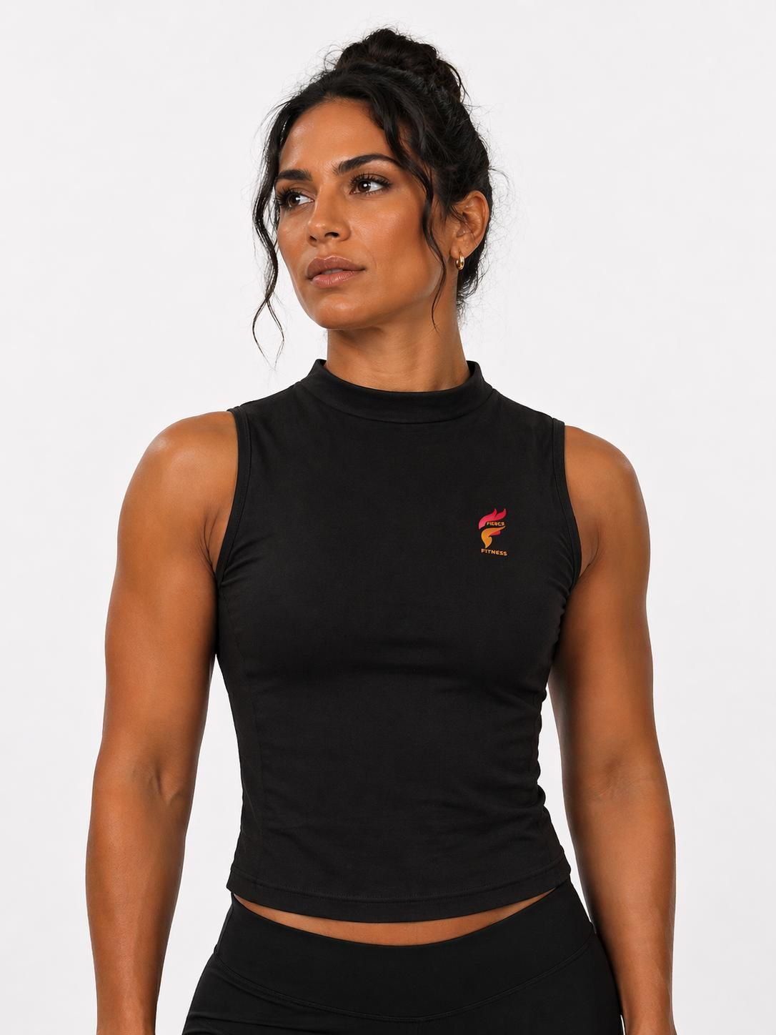 Woman in black sleeveless top standing against a white background, looking to the side.