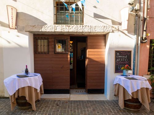 Ingresso del ristorante con porta in legno, due tavoli con tovaglie bianche e un cartello.