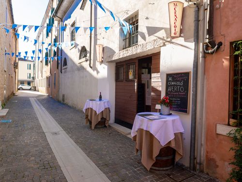 Stretta strada europea con ingresso del ristorante, tavoli e bandiere blu.