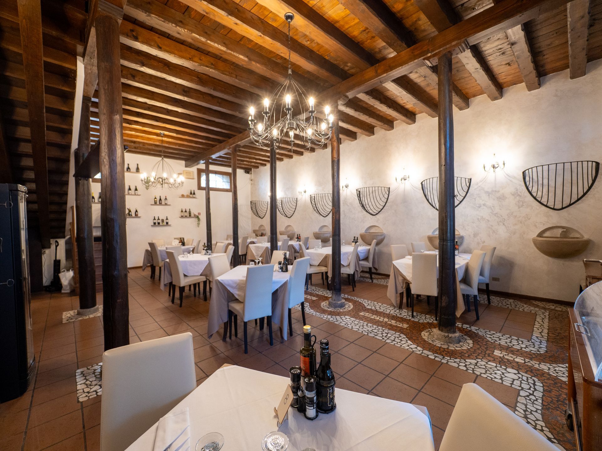 Interno del ristorante con tavoli con tovaglie bianche, sedie, travi in legno scuro e pareti decorate.