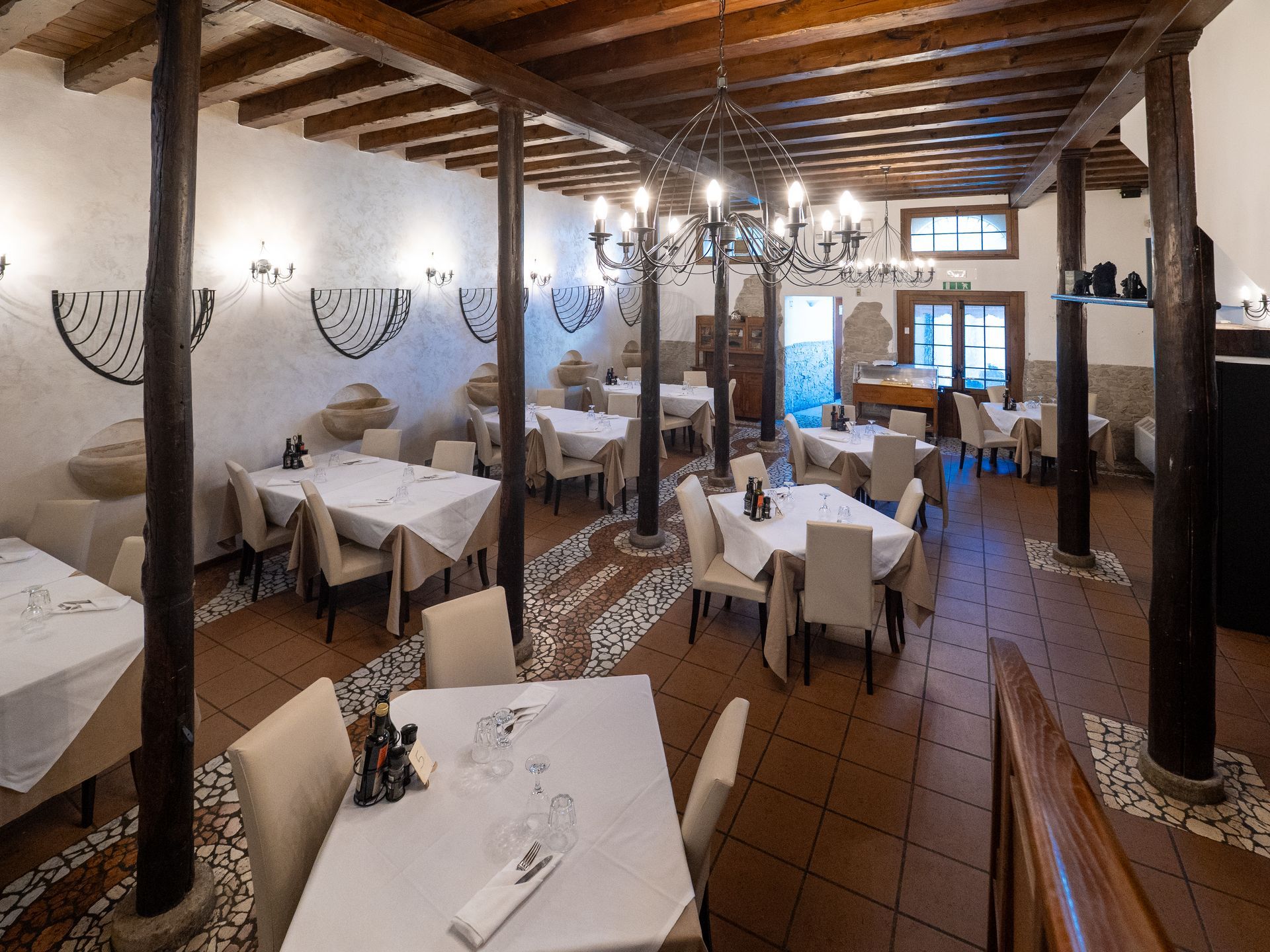 Interno del ristorante con tovaglie bianche, sedie color cuoio, travi in legno a vista e pavimento piastrellato.