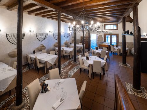 Interno del ristorante con tovaglie bianche, sedie color cuoio, travi in legno a vista e pavimento piastrellato.