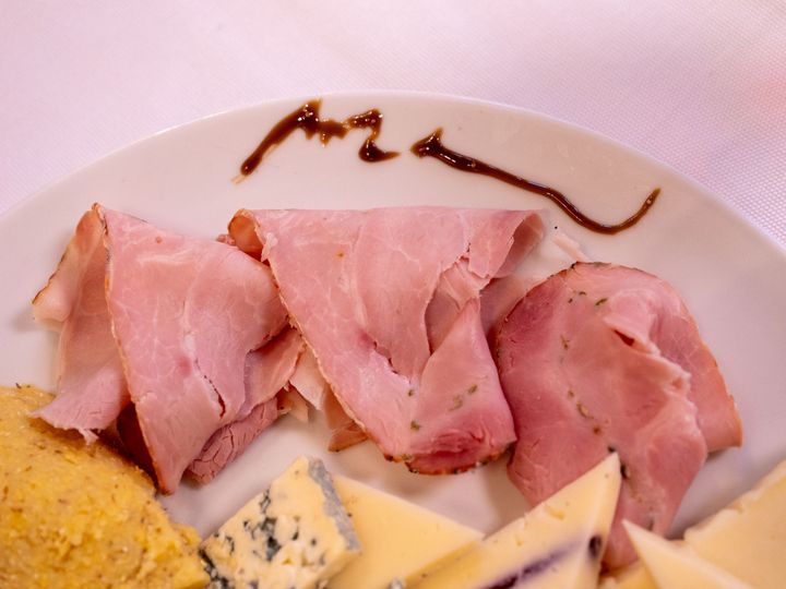 Fette sottili di prosciutto su un piatto bianco con formaggio e un filo di salsa.