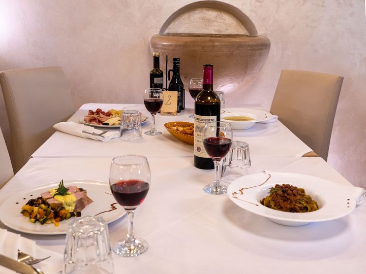 Tavolo da pranzo apparecchiato con cibo, vino e stoviglie in un ambiente da ristorante.