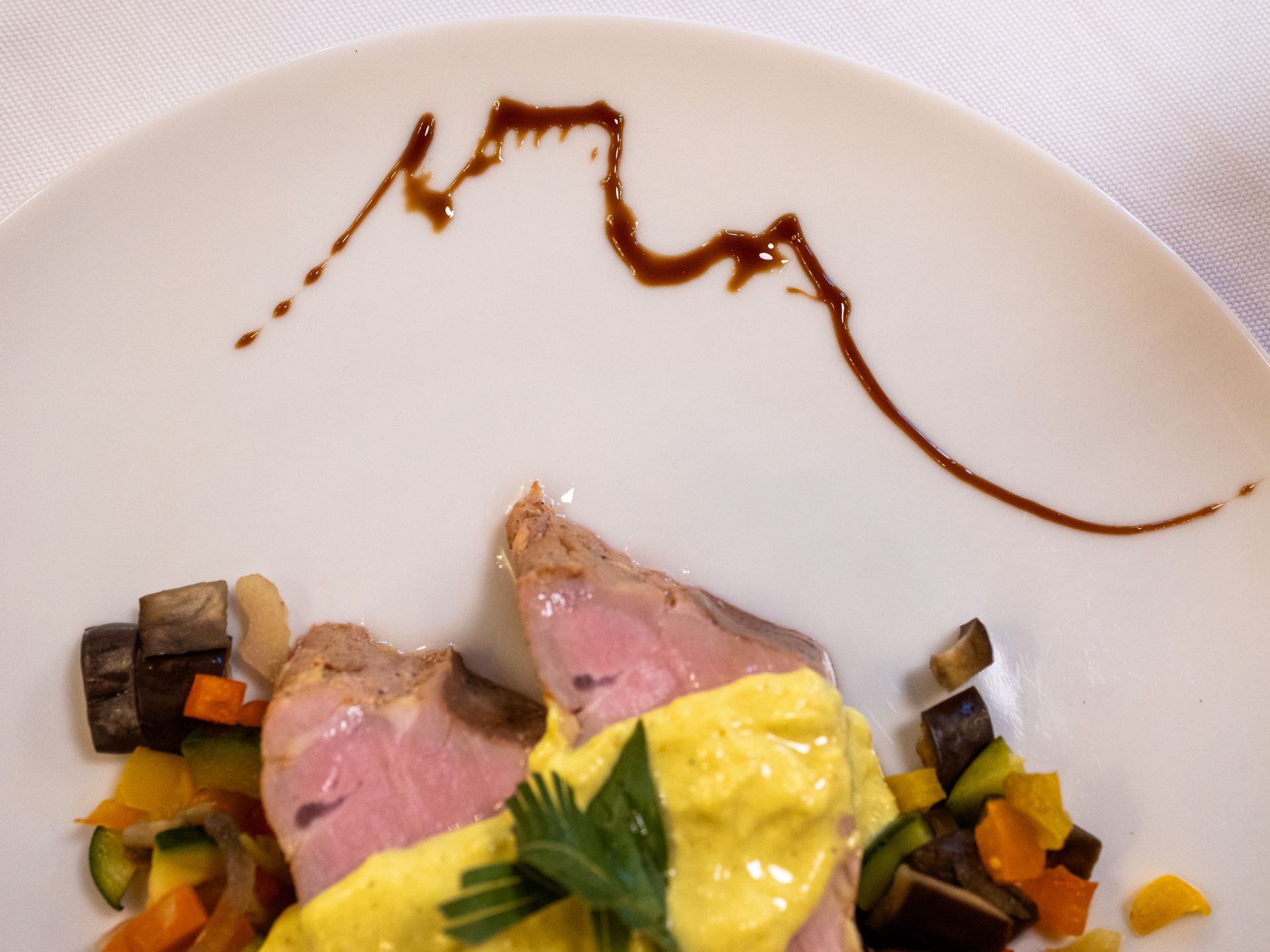 Carne affettata con salsa gialla, verdure e salsa su un piatto bianco.