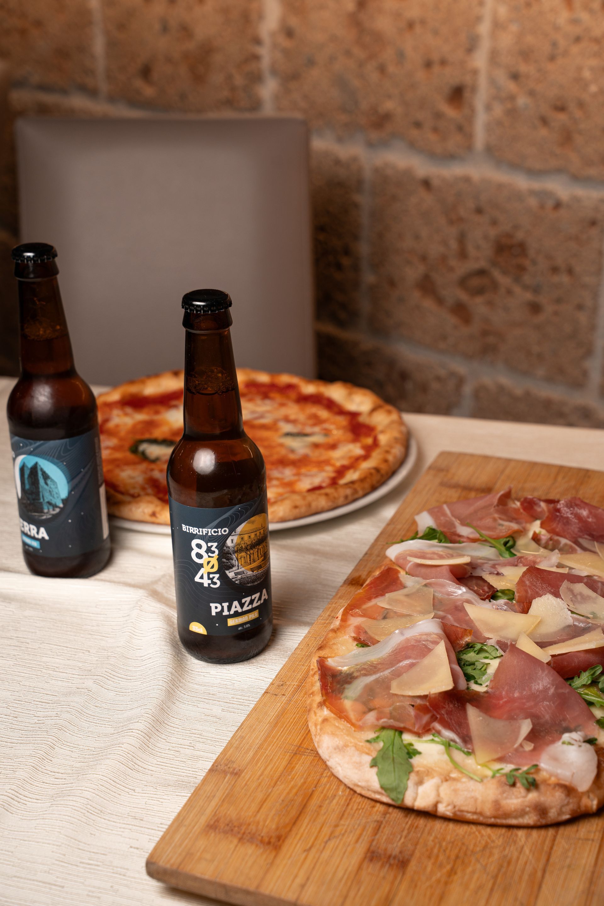 Bottiglie di birra, pizze e un tagliere di salumi su un tavolo.