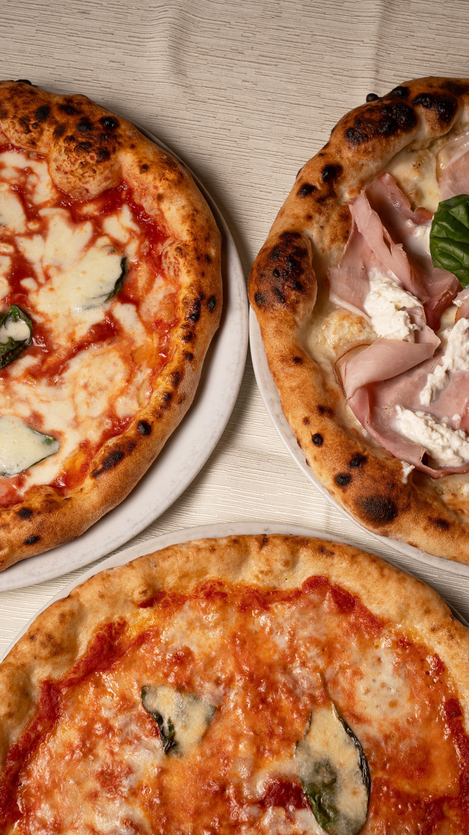 Tre pizze: Margherita, prosciutto e pomodoro, su una superficie ruvida.
