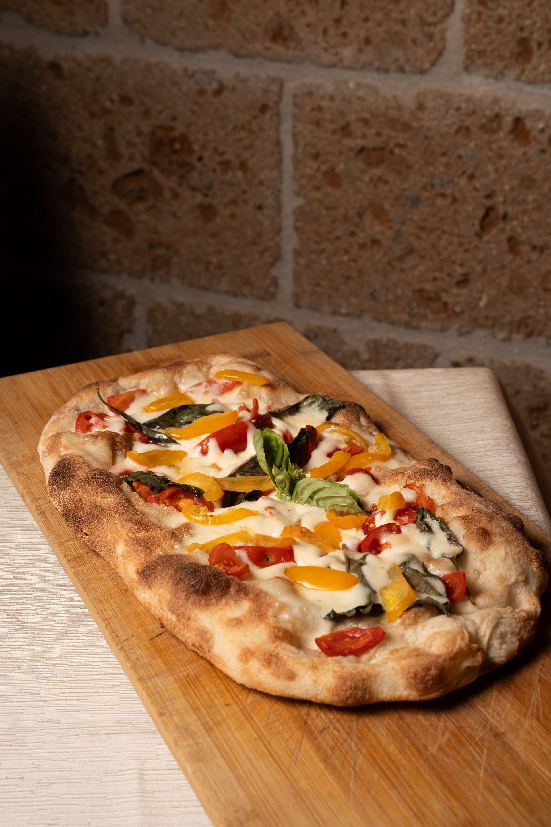 Pizza vegetariana su una tavola di legno contro un muro di mattoni.