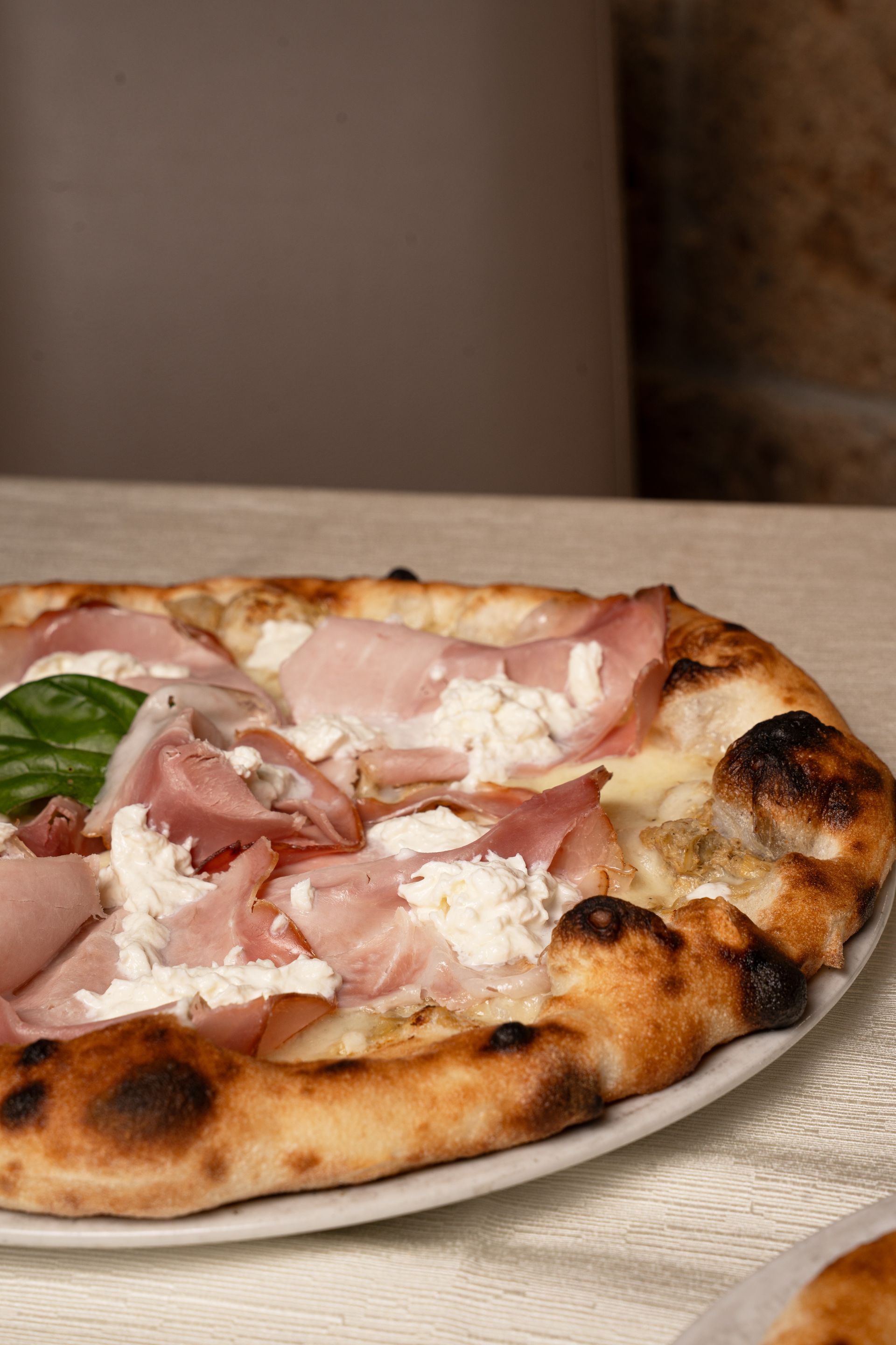 Pizza con prosciutto e ricotta su un piatto bianco.