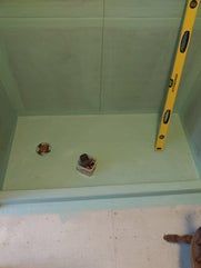 Shower stall construction with level, drain, and plumbing visible; green foam construction.