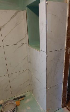 Tile work in progress. White marble-look tiles installed on bathroom wall, with recessed niche and green backing.