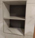 Two-tiered bathroom shelf built into a wall. Gray frame, mesh backing, white interior.