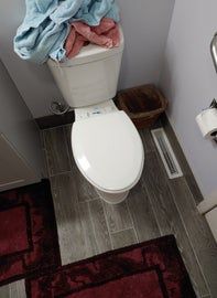 Toilet with towels on top, in a bathroom with dark wooden floor, red rugs.