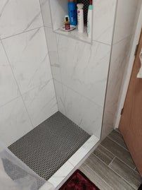 Shower with white marble-look tile walls, dark mosaic tile floor, built-in shelf holding toiletries.